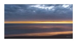 Photographie d’art montrant un horizon marin au coucher de soleil, avec une bande lumineuse dorée sous un ciel nuageux, œuvre de la série Horizons lumineux.